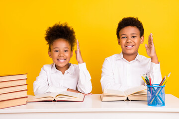 Fototapeta premium Photo of young positive dark skin people siblings sit desk school raise hands books isolated on yellow color background