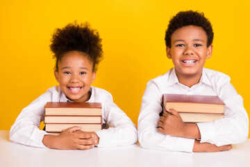 Photo of cheerful young dark skin friends children sit table hold books smile isolated on yellow...