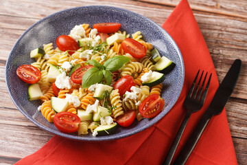 Italian pasta fusilli tricolore with cherry tomatoes, zucchini and feta cheese in a blue shallow...