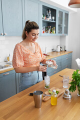 culinary, drinks and people concept - happy smiling young woman making lime mojito cocktail at home kitchen