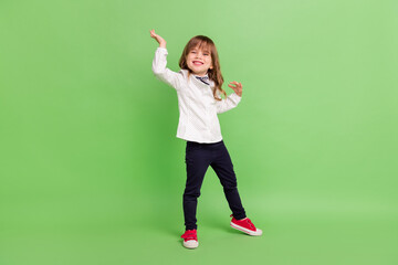 Full length photo of little funny girl dance wear white shirt trousers sneakers isolated on green color background