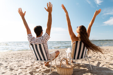 leisure, relationships and people concept - happy couple with picnic basket sitting in folding...