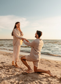 love and people concept - smiling young man with engagement ring making proposal to happy woman on beach