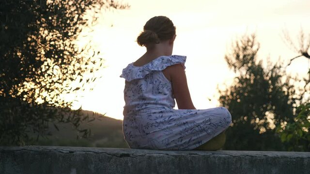 Beautiful Young Causian Girl Sitting on Terrace Wall in Tuscan Villa Looking at Golden Sunset during Summer Vacations Holidays