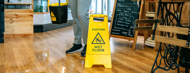 Worker placing wet floor sign after mopping the floor - obrazy, fototapety, plakaty