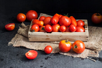 Fototapeta na wymiar Fresh red tomatoes in wooden box on black background