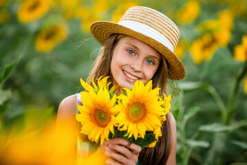 A beautiful happy little girl holds a bouquet of flowers in a field of sunflowers. Summer cozy mood.