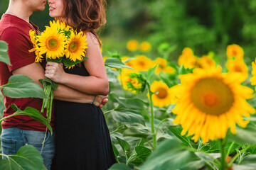 A beautiful young couple a man and a woman, embrace in a field of sunflowers at sunset. The concept...