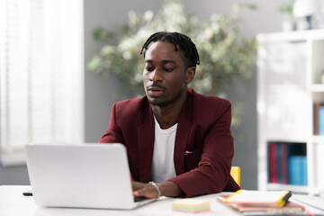 Focused corporate employee sits in office in afternoon working on new project, dark-skinned man...
