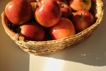 Ripe red apples in a straw basket with shadows on light background at home