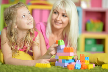 Obraz na płótnie Canvas little daughter and mother playing with colorful plastic blocks at home