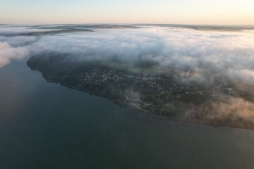 Aerial view of large river with fog above the water.  Colorful landscape with forest in low clouds, river, meadow in fog, orange sky with sun in the morning. .Top view. Nature