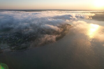 Aerial view of large river with fog above the water.  Colorful landscape with forest in low clouds, river, meadow in fog, orange sky with sun in the morning. .Top view. Nature