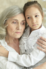 portrait of sad grandmother and granddaughter hugging at home