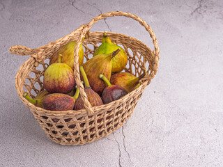 A pile of ripe figs fruit is in a bamboo basket on a cement floor background. High Vitamins fruit. Space for text. Healthy fruits and healthcare concept