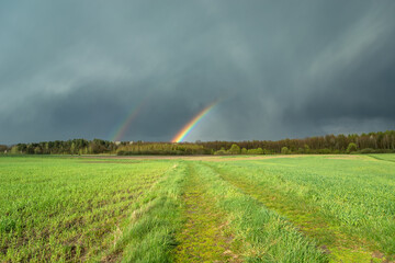 Cloudy sky with a fragment of a rainbow and a green meadow