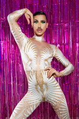 young drag queen with short hair and mustache posing with fuchsia color background