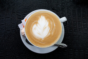 cappuccino with a flower pattern in a white cup on a black background