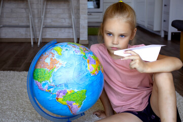 cute girl 7 years old of European appearance with blue eyes and blond hair hugs the globe, plays with a paper plane, early education through the game