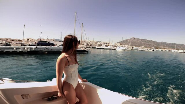 Young woman enjoying the view of Puerto Banus port on the yacht. Sailing a yacht on slightly wavy sea. Sailing with a skipper. 