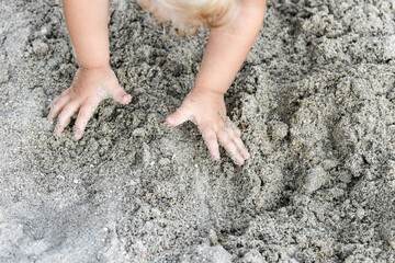 The child collects wet sand all in a heap to build something.