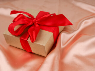 Gift box with a red bow on a silk nude fabric