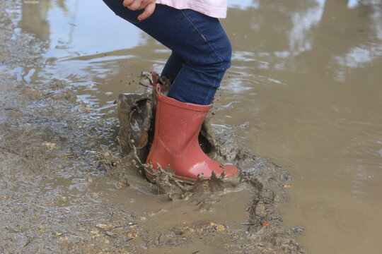 Ni&ntilde;a saltando en un charco de barro salpicando con botas de agua