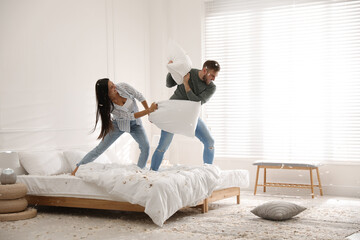 Happy young couple having fun pillow fight in bedroom - Powered by Adobe