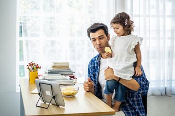 Young attractive father and little cute daughter watching the movie video or cartoon on the tablet and eating potato chips at home with happiness.
