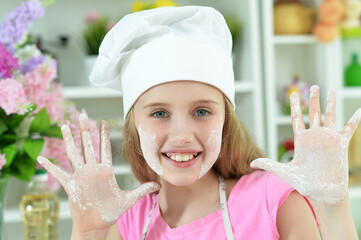Cute girl in chefs hat showing palms covered with flour