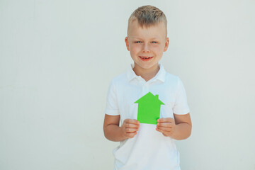 Children's hands holding a house made of green paper. concept of ecological houses