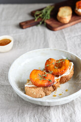 Summer Breakfast - toast (sandwich, bruschetta) with grilled peaches, cream cheese (ricotta, mascarpone), thyme and honey on beige linen tablecloth. Selective focus