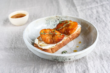 Summer Breakfast - toast (sandwich, bruschetta) with grilled peaches, cream cheese (ricotta, mascarpone), thyme and honey on beige linen tablecloth. Selective focus