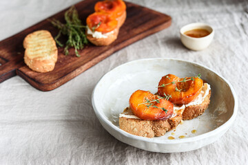 Summer Breakfast - toast (sandwich, bruschetta) with grilled peaches, cream cheese (ricotta, mascarpone), thyme and honey on beige linen tablecloth. Selective focus