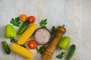 food and culinary background with copy space for text top view, pepper mill, pink himalayan salt and cooking ingredients, fresh vegetables tomatoes, cucumbers  on the kitchen wooden table