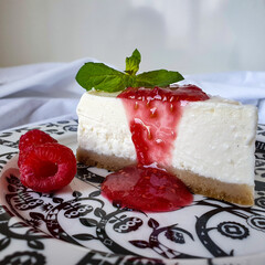 Piece of cheesecake with raspberries and jam on black and white plate