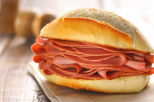 sandu&iacute;che de mortadela no p&atilde;o franc&ecirc;s sobre superf&iacute;cie de madeira r&uacute;stica 