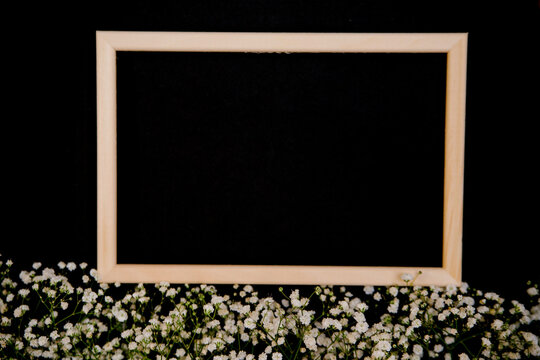 Photo frame and small white flowers on a black background. The white flowers of the gypsophila lie in a row.