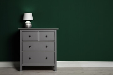 Modern chest of drawers with lamp near green wall indoors. Space for text