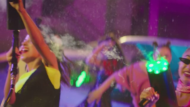 Mini smoke machine on the hand of beautiful sexy crazy girl . Girls dancing , partying inside abandoned garage with old vintage cars . Dry Fog device in hand . Female dancer spraying smoke all around
