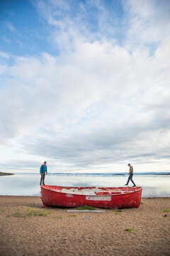 Two men standing on the edge of old boat on beach in Iqualuit, Canada