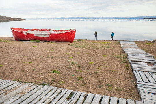 Travelers stand on the shore next to red boat in Apex, Iqualuit.