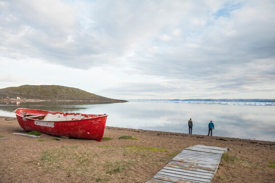 Two men stand on the shoreline looking at icebergs in Iqaluit, Canada