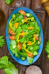 fresh summer green salad with vegetables cucumber, tomato, bell pepper, and leaf lettuce in ceramic bowl, dieting and vegan food on wooden background