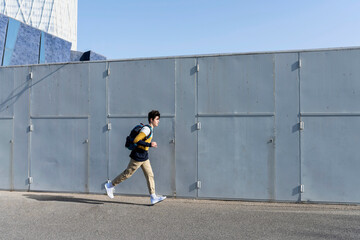 Young teen running beside a wall with backpack