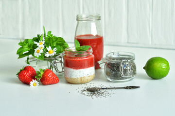 Homemade cheesecake with strawberry and cottage cheese cream in a glass jar.fresh green lime, mint and chia on white background.summer dessert without baking