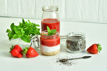 Homemade cheesecake with strawberry and cottage cheese cream in a glass jar.fresh green lime, mint and chia on white background.summer dessert without baking