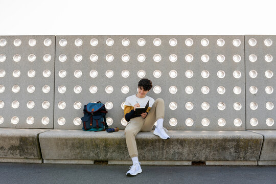 Young male writing notes in a notebook sitting on a bench
