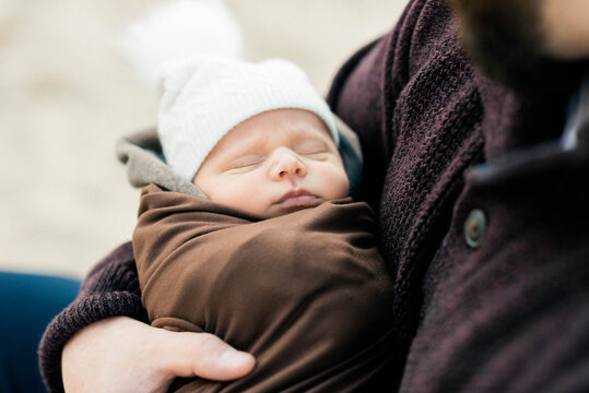 A Newborn Baby Bundled Up And In His Father's Arms