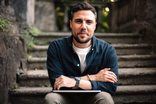 Portrait of happy man with laptop sitting on steps in city